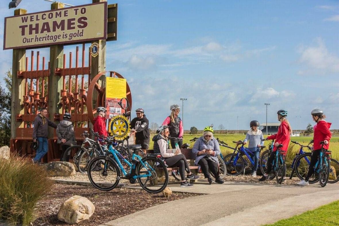 Group of cyclists resting by a 'Welcome to Thames' sign
