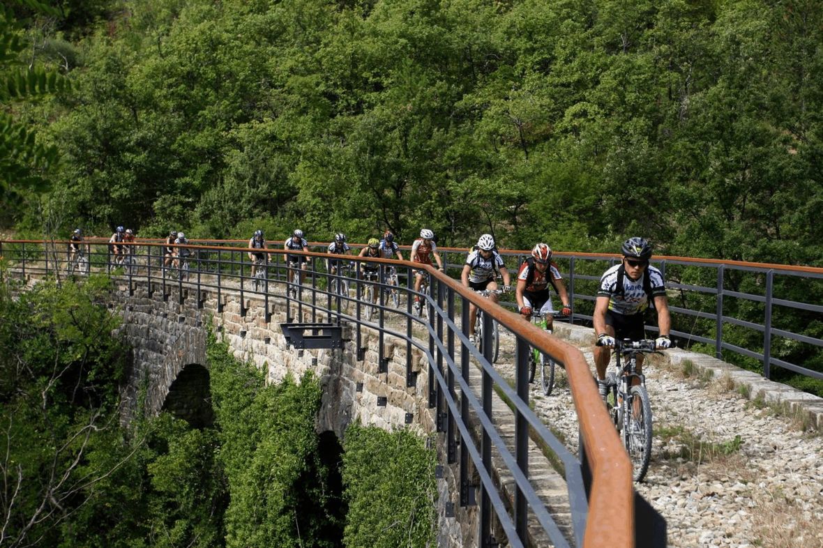 Line of cyclists riding over historic bridge