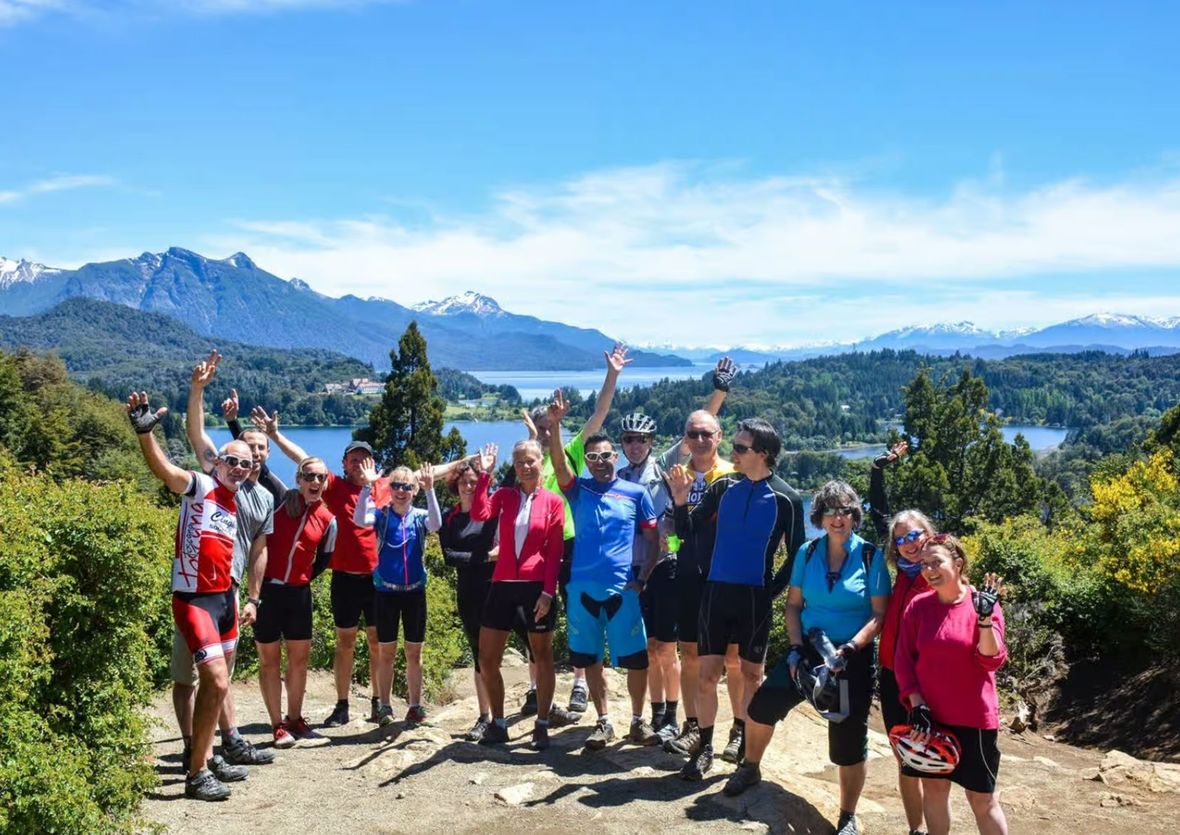 Group waving and smiling on hill above lakes and mountains