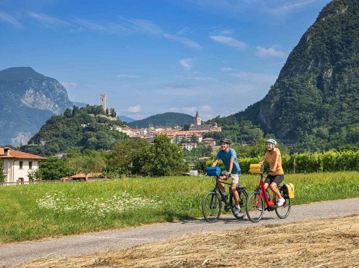 Two cyclists on path in green countryside with historic villages and mountains