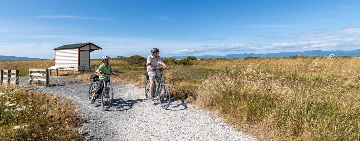 Two cyclists on path looking out towards ocean