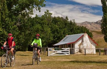 Couple cycling by small white cottage