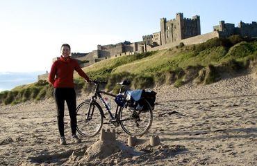 Cyclist on beach with bike and castle backdrop