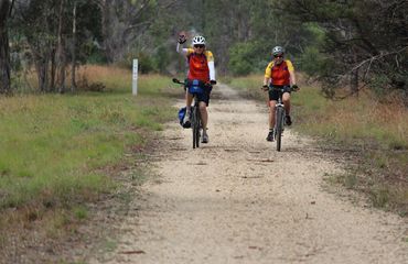 Couple of cyclists waving and riding on countryside track