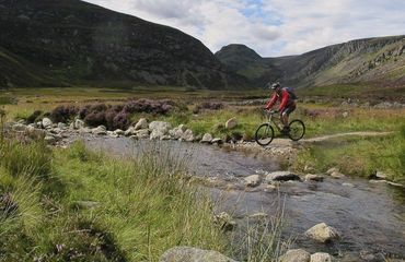Cyclist riding across water with mountainous backdrop