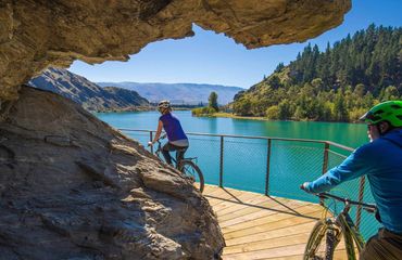 Cyclists riding on a boardwalk with rocky overhang by water