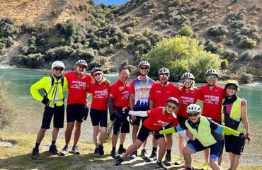 Group of cyclists off the bikes posing for photo by water