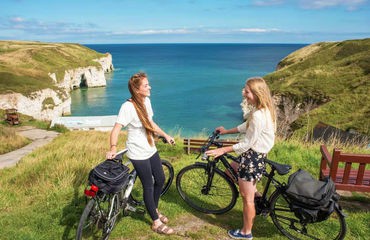 Two female cyclists resting on their bikes on top of a cliff with sea in background