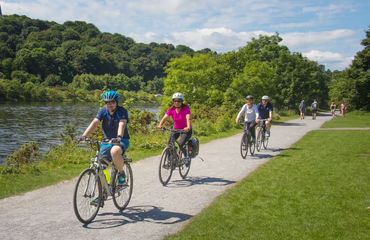 Group of cyclists riding along pathway next to water