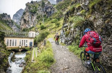 Cyclists riding along a track by the water, in the mountains