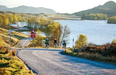 Cyclists riding up hill by water