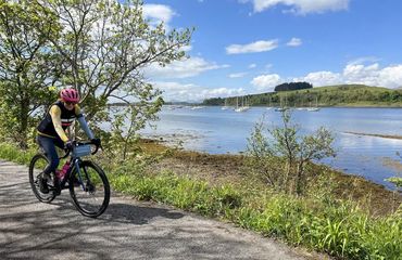 Cyclist riding in dappled shade by water