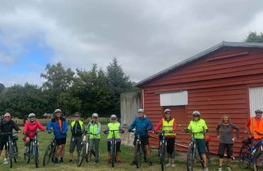 Group of cyclists standing with bikes by big red shed