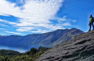 Person standing on rocky outcrop overlooking lake and mountains