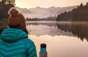 Person with flask looking out over lake and misty mountains