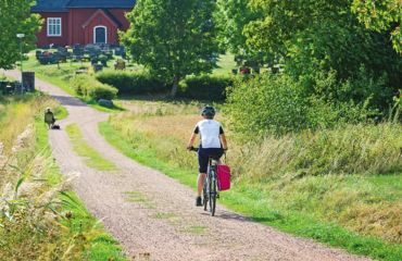 Cyclist riding towards a red building on a countryside lane