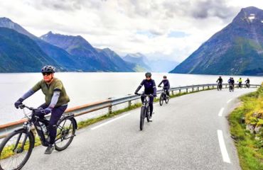 Cyclists in a group on a road next to fjords and mountains