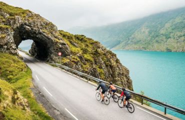 Cyclists on road riding through mountain tunnel by water