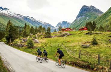 Cyclists riding next to green fields with mountain backdrop