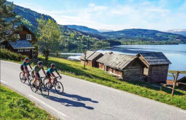 Cyclists on road by lake and cabins