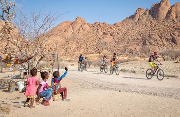 Children waving to cyclists as they ride by in desert landscape