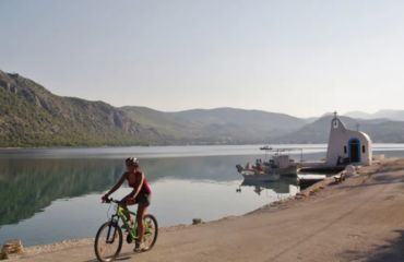 Cyclist riding past water and white small building