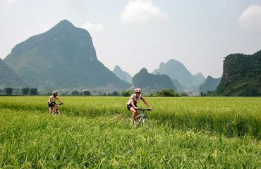Cyclists riding through fields with mountains behind