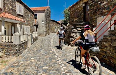 Two cyclists riding up cobbled street through stone village