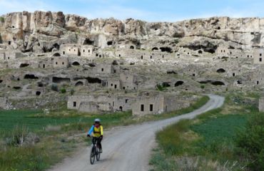 Cyclist riding away from cave dwellings on quiet road