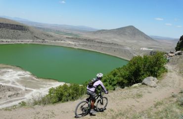 Cyclist on dirt road overlooking lake and mountain