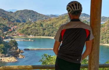 Person in cycle helmet looking out to sea with forested hills
