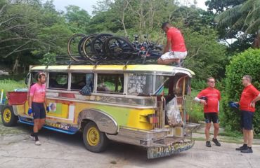 Colourful small bus with bikes on roof and people standing by