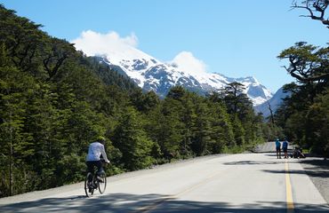 Cyclists riding along road with snow capped mountains in background