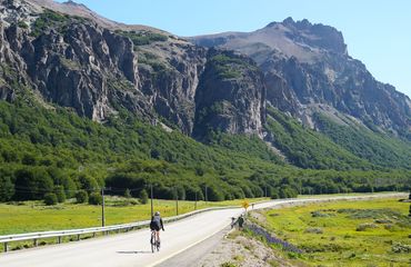 Cyclist on road past mountains
