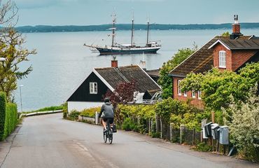 Cyclist riding down road to the water with sail boat in shot