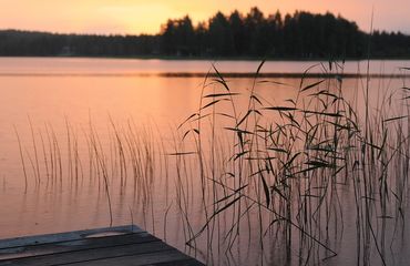 Lake with wooden jetty and forested island at sunset