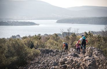 Mountain bike group riding down rocky path towards sea