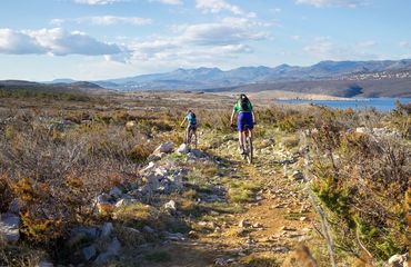 Cyclists riding down rural track with sea and mountains in the distance