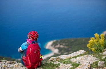 Cyclist off the bike sitting on edge of rocks looking out to blue sea
