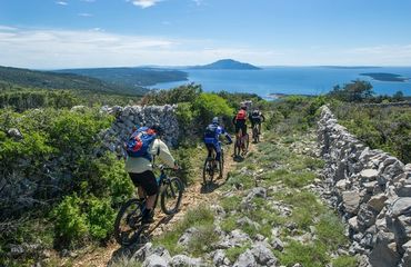 Cyclists riding along rock-walled pathway to sea