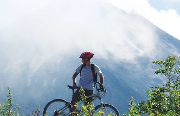 Cyclist standing in front of volcano in fog