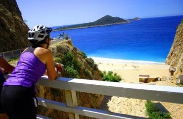 Cyclist leaning over fence and looking out at ocean and beach