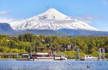 Snow-capped volcano rising above greenery and lake foreground