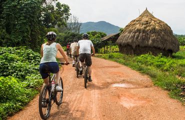 Cycling on red dirt path past straw buildings