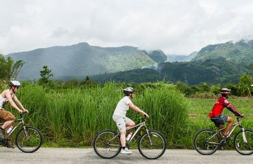 Cyclists riding past fields and mountains
