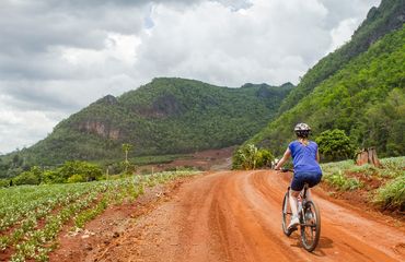 Cyclist on red dirt road with mountains in distance