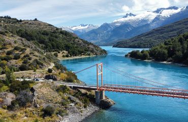 Red bridge over blue lake with snow capped mountain backdrop