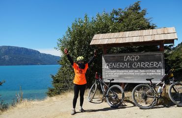 Cyclist off the bike with hands in air at lakeside