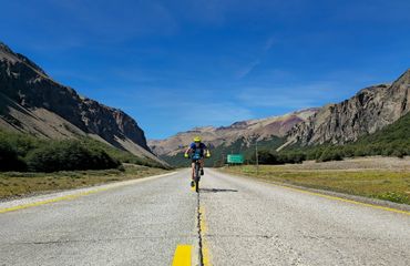 Cyclist riding down middle of the road with mountains on either side