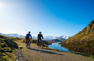 Two cyclists on trail with river to one side and hills in the back
